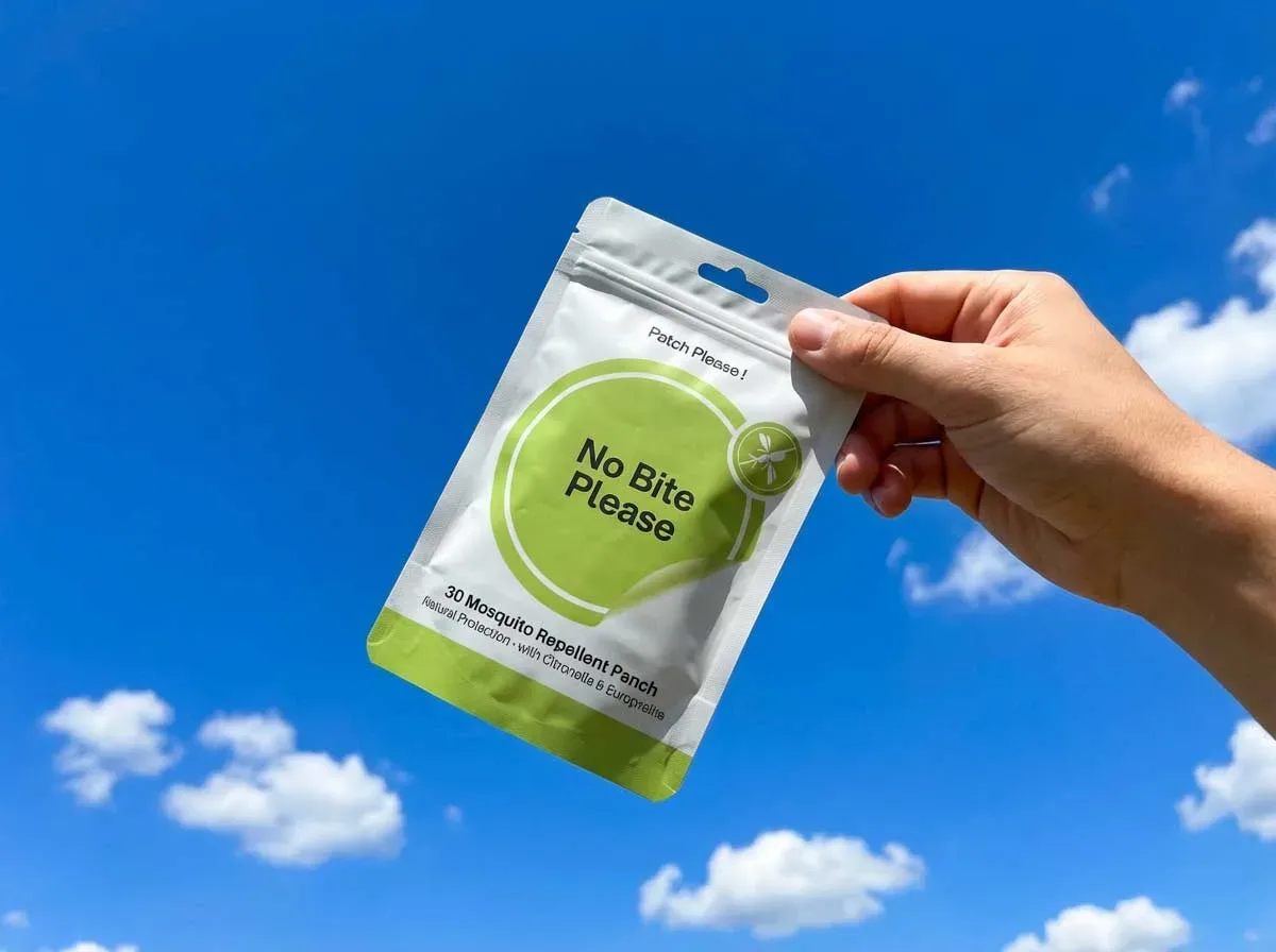 No Bite Please mosquito repellent patch package displayed with individual patches visible, showing the small circular patches with natural ingredient labeling, outdoors setting with blurred camping background